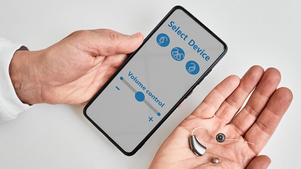 Audiologist holding hearing aid and smart phone with hearing app
