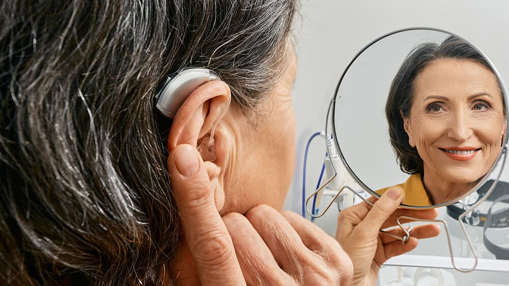 Mature woman holding her finger on her ear with BTE hearing aid