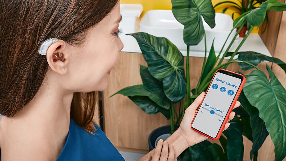 Woman with hearing aid holding smart phone and adjusting the settings of her hearing aid app