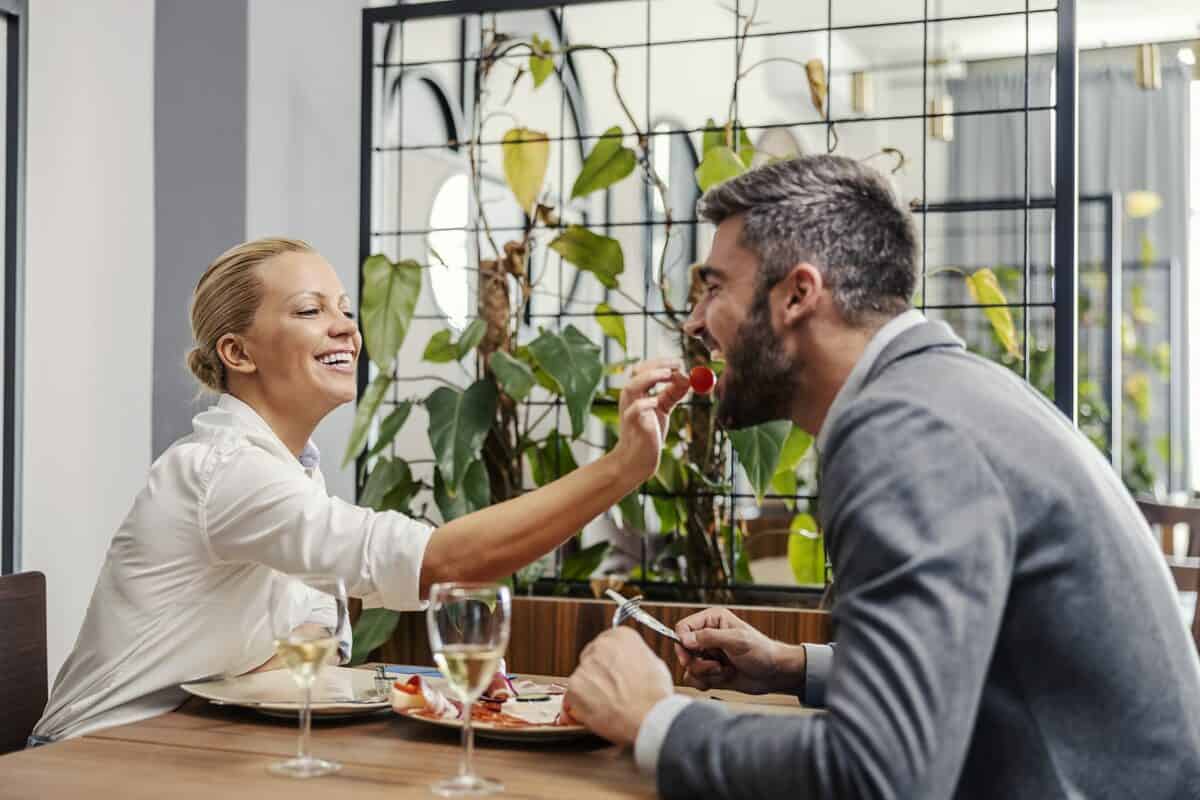 Woman putting small tomato in man's mouth at lunch