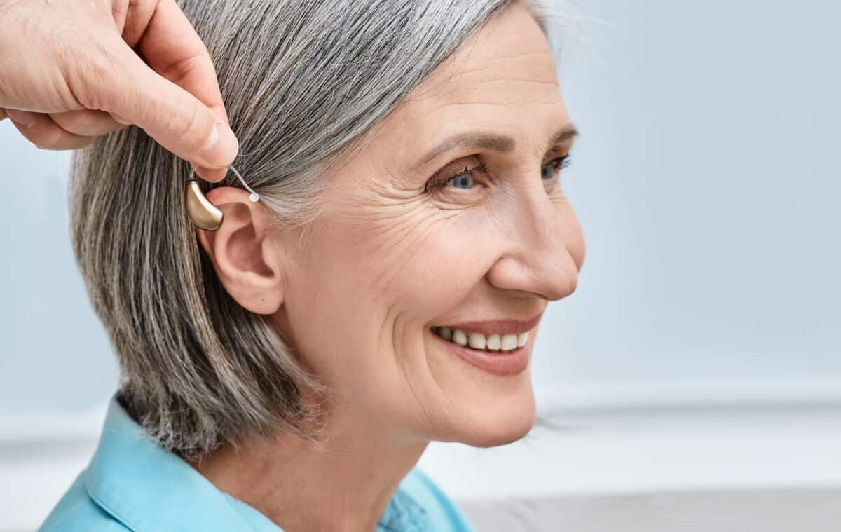 Elderly woman smiling with hand holding a hearing aid by her ear